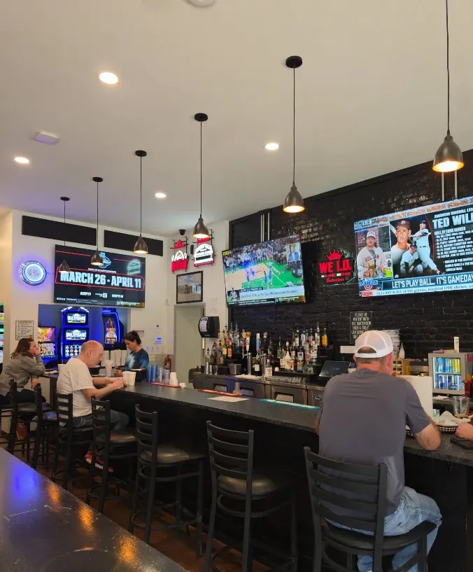 Placeholder photo: the bar and dining room with TVs and a few customers, shown blurred